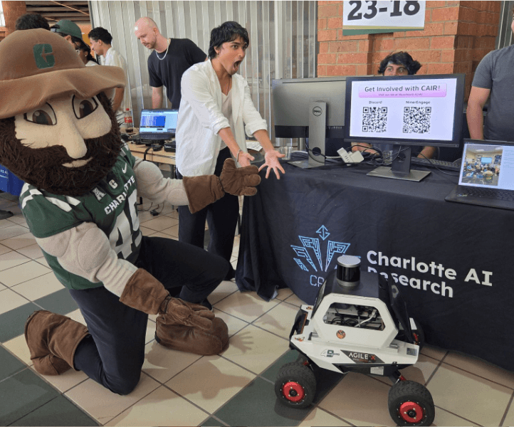 Rafan at a Charlotte AI Research table with a mascot and a small robot